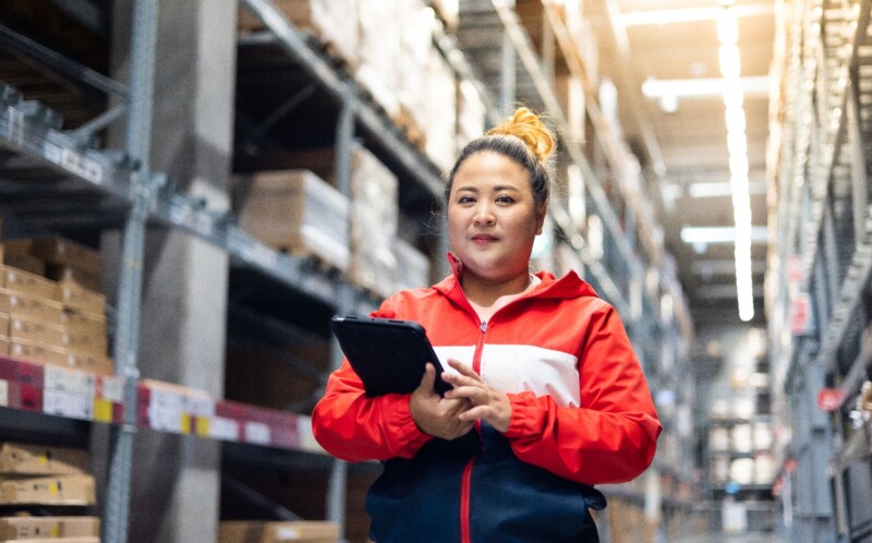 Female worker inspecting box of products while working in large warehouse